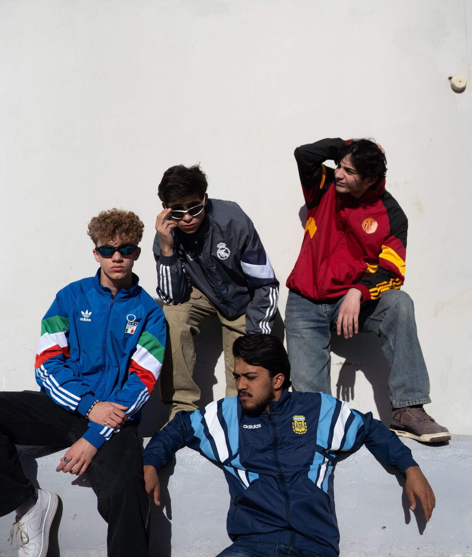 Four young men wearing stylish sports jackets posing outdoors on a sunny day.